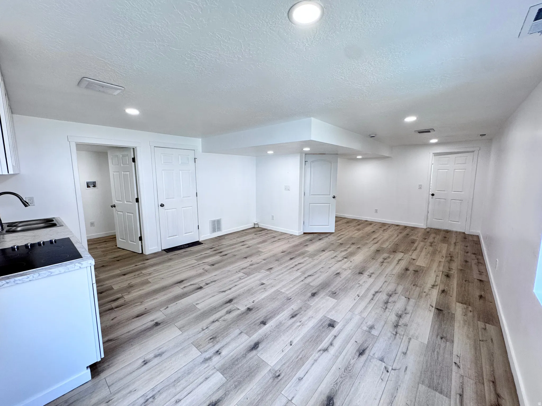 Finished below grade area with light wood-style flooring, a textured ceiling, and recessed lighting