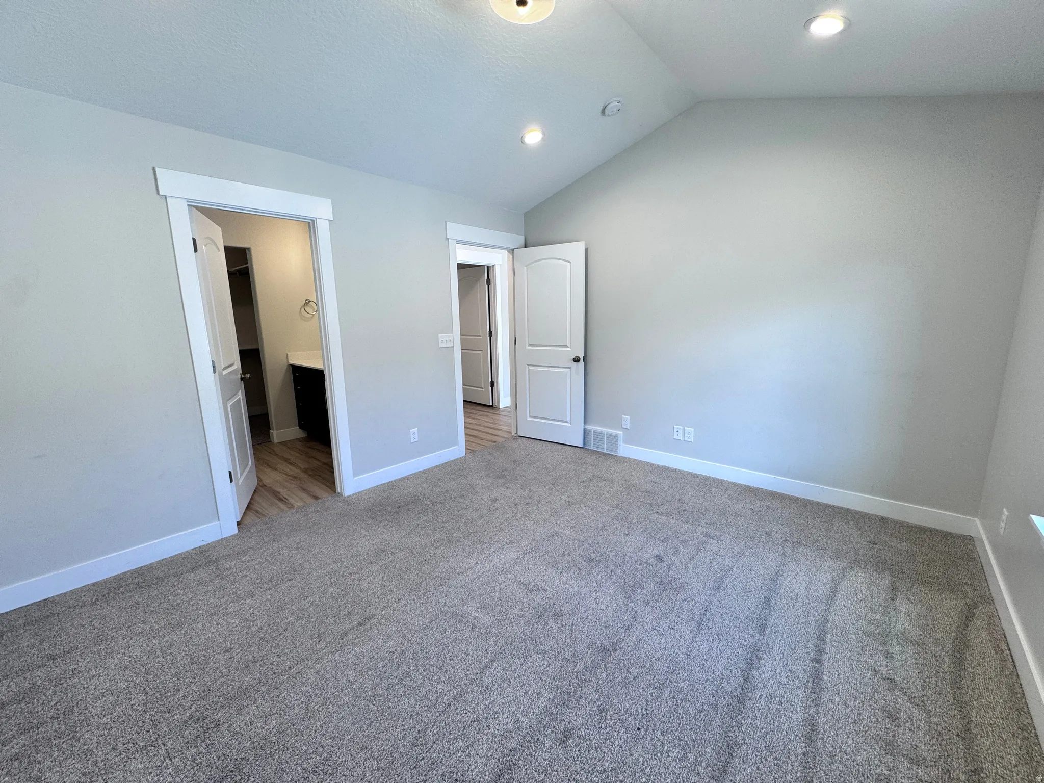 Unfurnished bedroom featuring vaulted ceiling, ensuite bathroom, carpet flooring, and recessed lighting