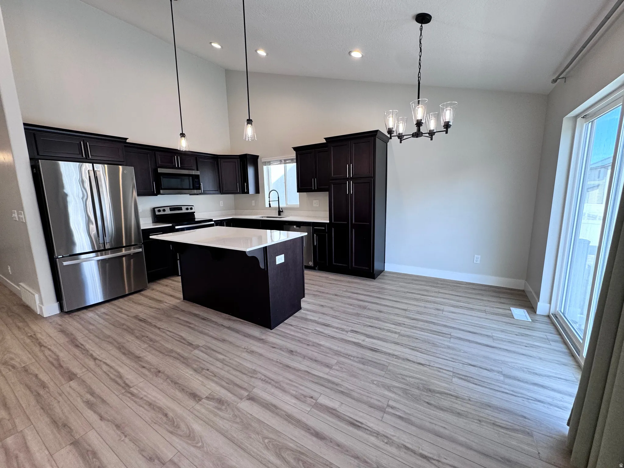 Kitchen featuring stainless steel appliances, suspended lighting, a center island, lofted ceiling, and light wood-style floors