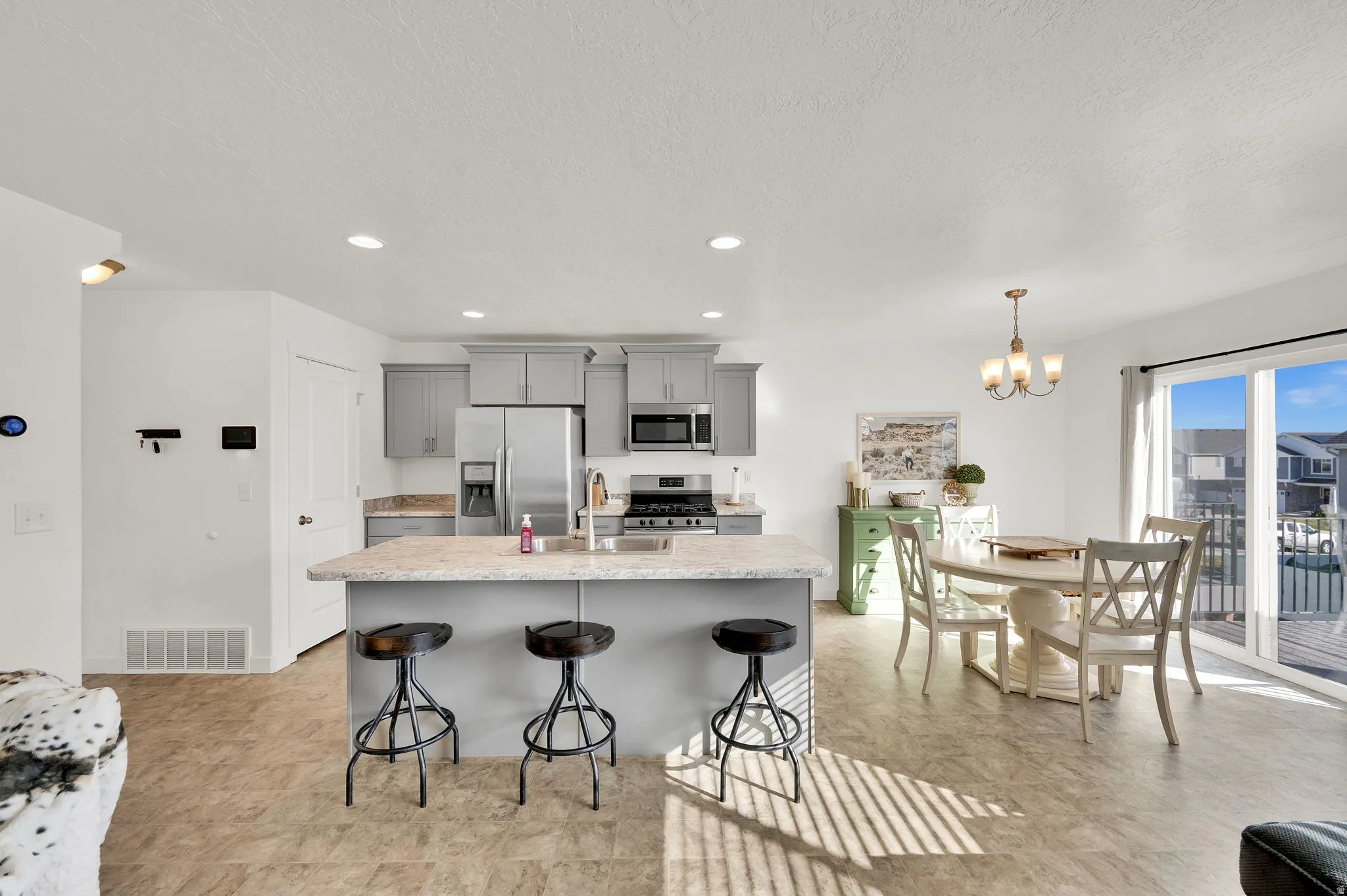 Kitchen with gray cabinets, stainless steel appliances, a breakfast bar, an island with sink, and a textured ceiling