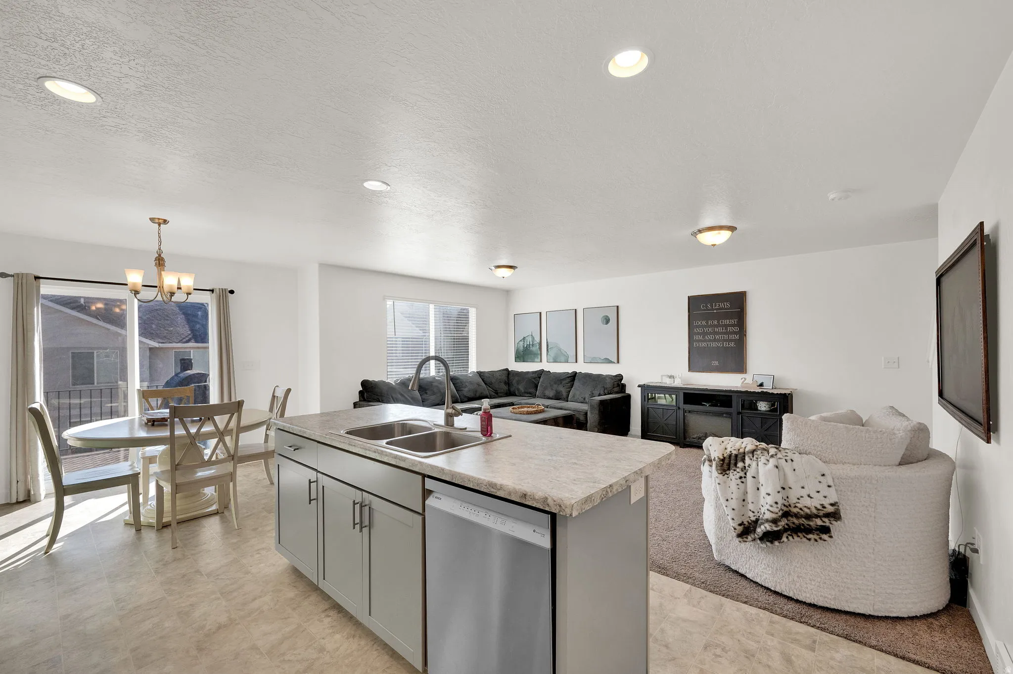 Kitchen featuring open floor plan, an island with sink, light countertops, dishwasher, and a chandelier