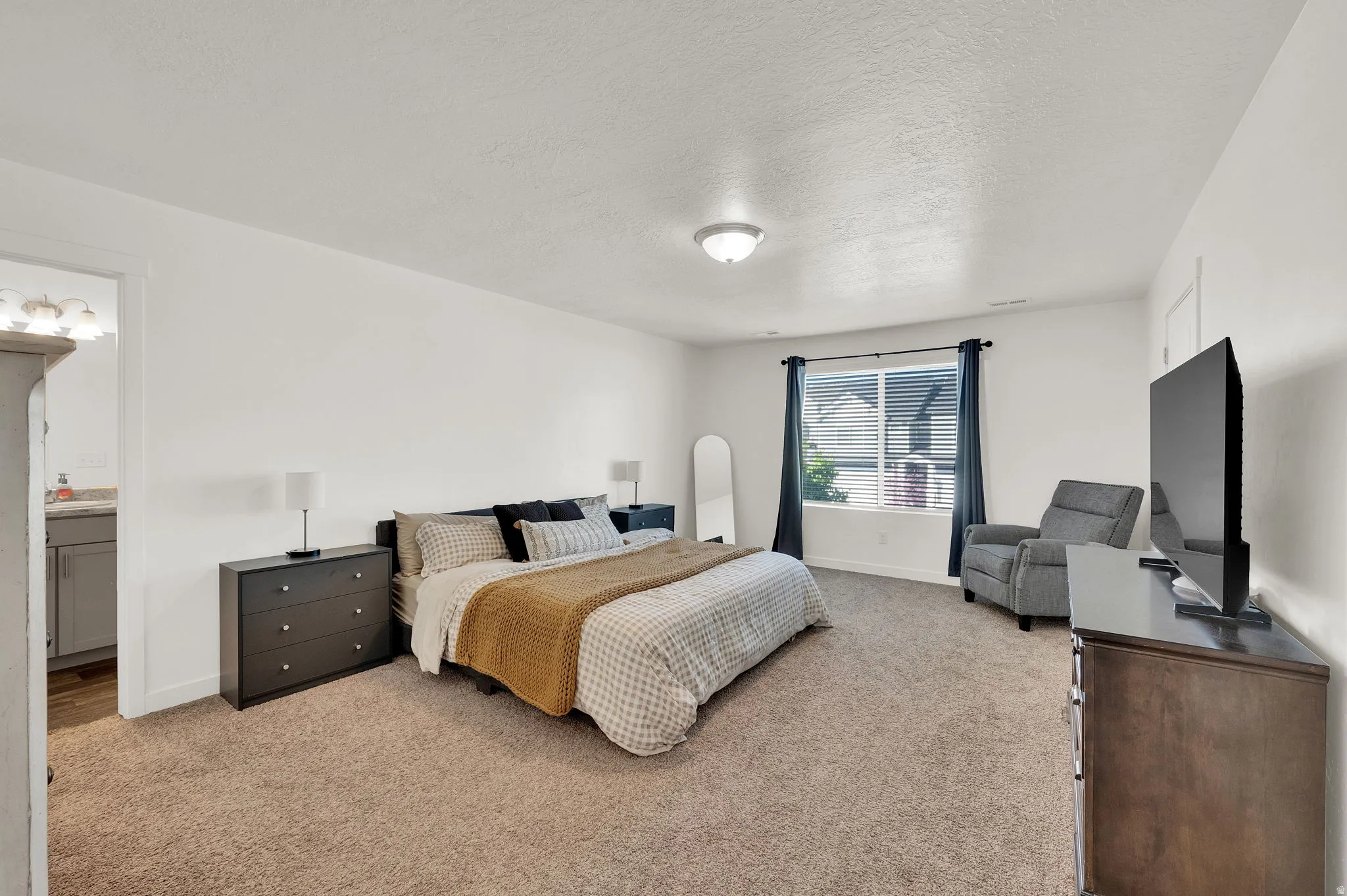 Bedroom featuring a textured ceiling, light colored carpet, and ensuite bath