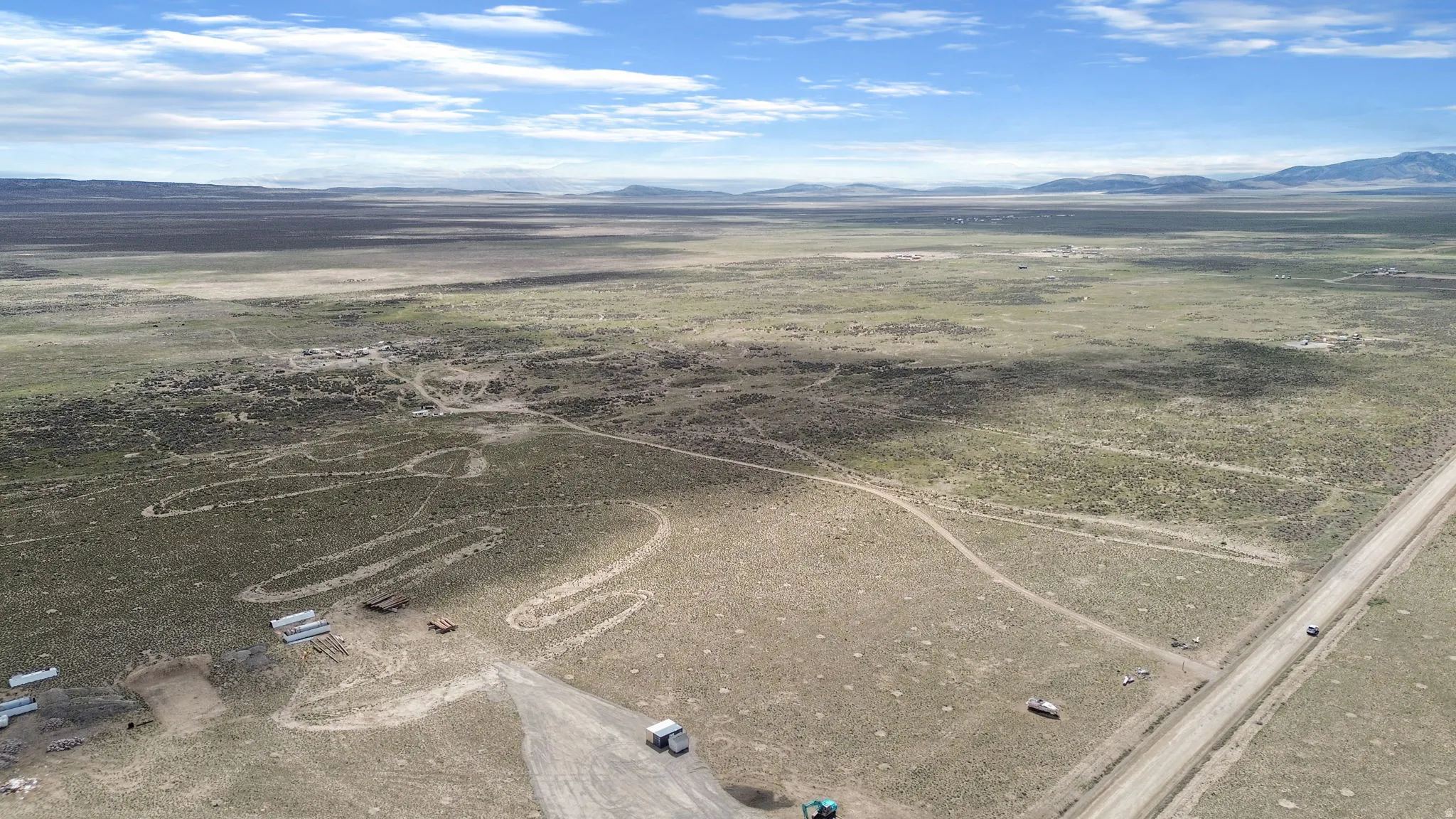Expansive open land featuring diverse vegetation, a clear blue sky with scattered clouds, and distant mountain ranges