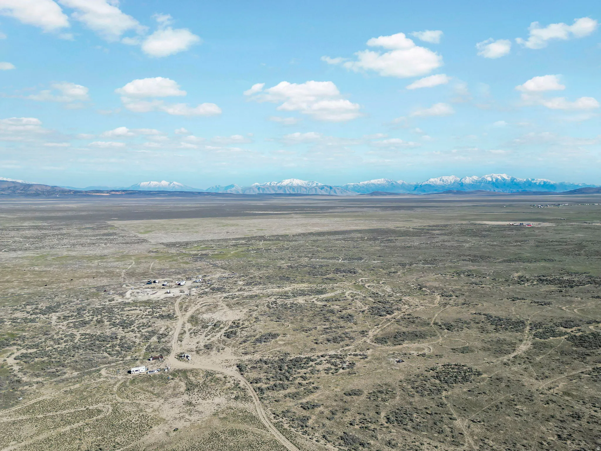 Expansive desert landscape with distant snow-capped mountains under a clear sky with scattered clouds