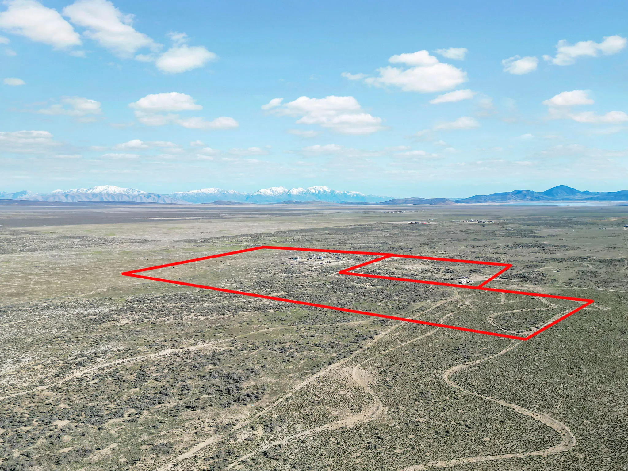 Expansive desert acreage featuring defined property lines, scattered natural vegetation, distant mountain range, and a broad sky overhead