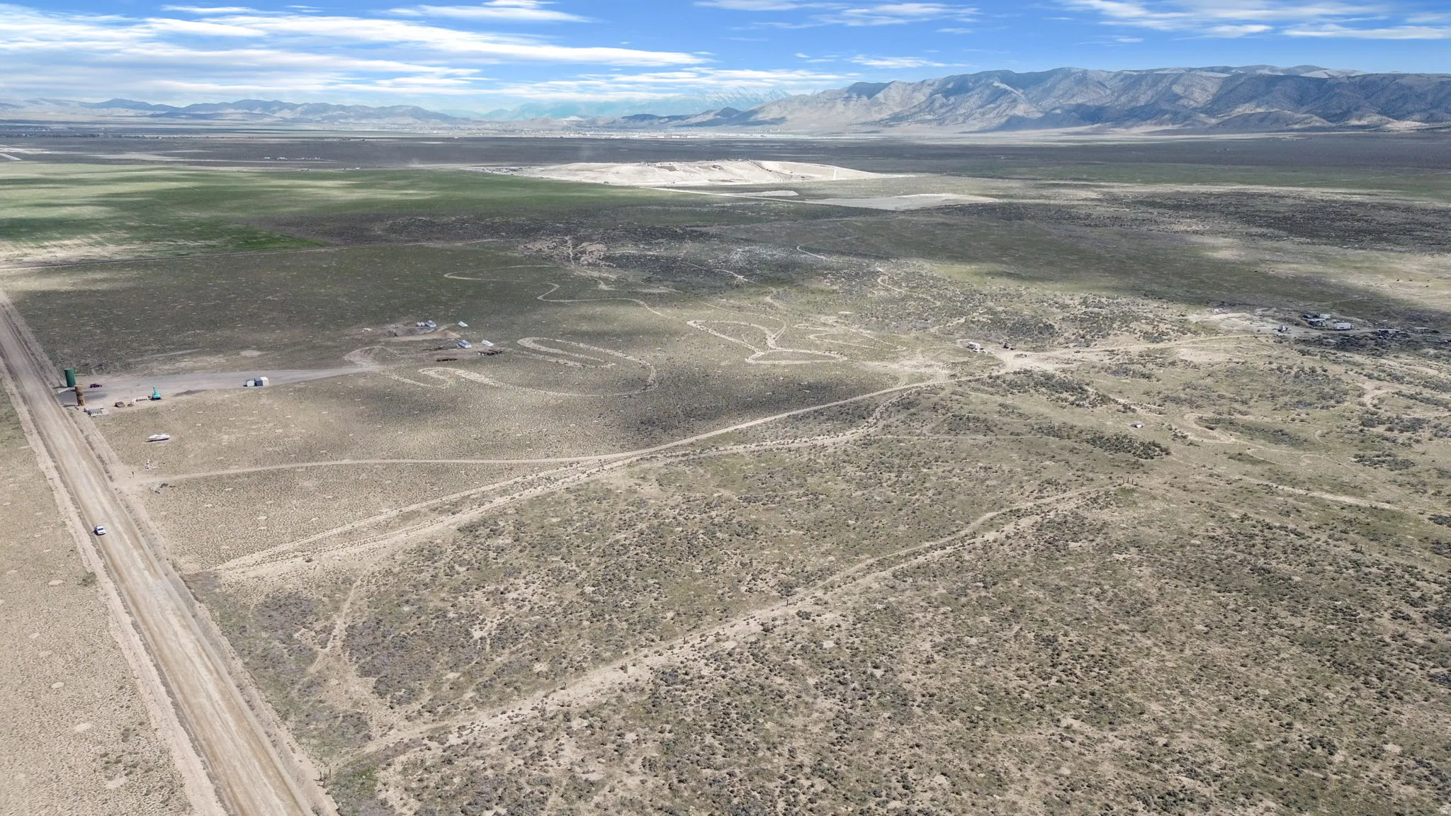 Expansive desert landscape featuring a dirt road, sparse vegetation, and distant mountains under a blue sky with clouds