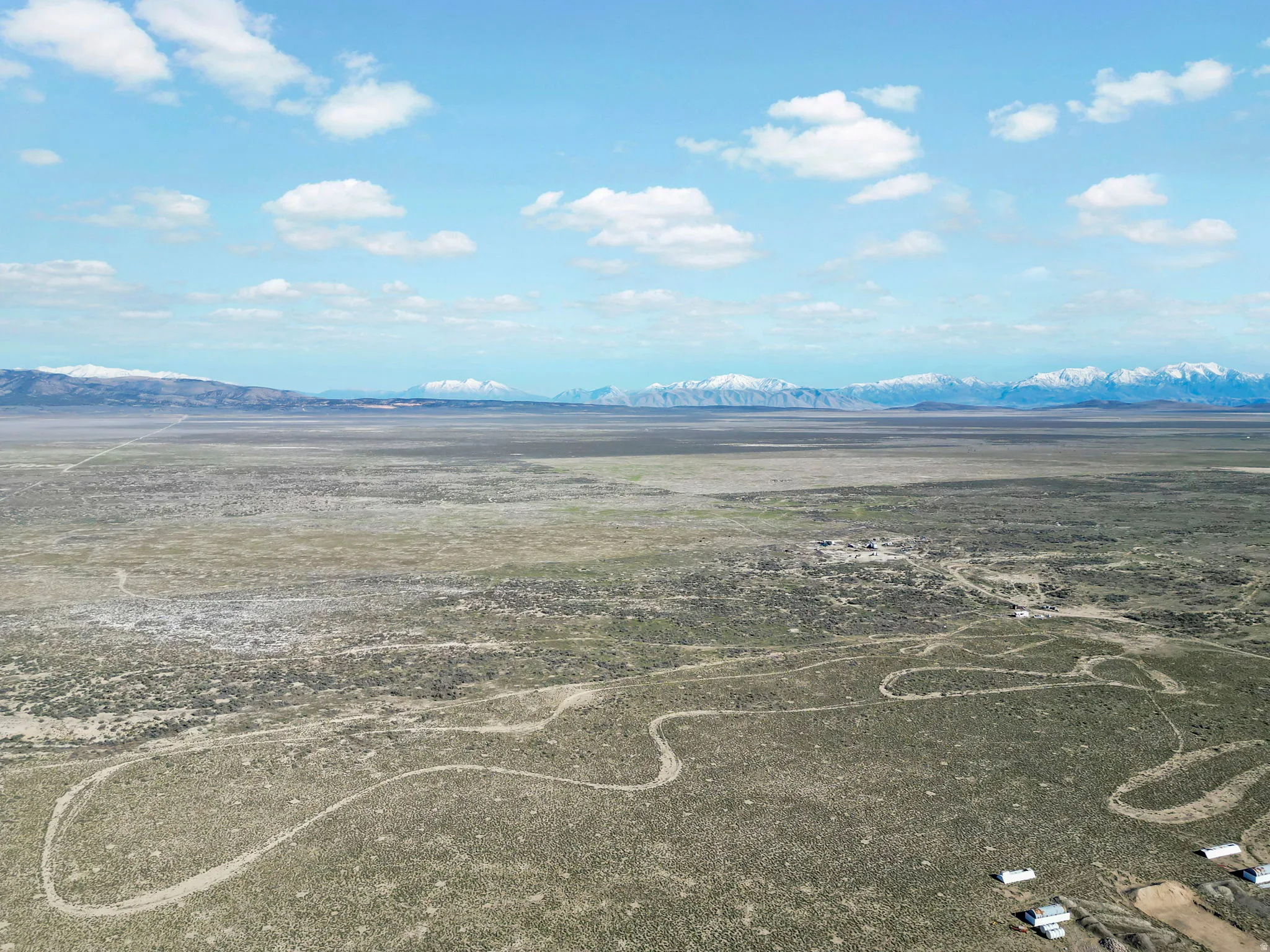 Expansive undeveloped land featuring a dirt track, distant snow-capped mountains, and scattered brush