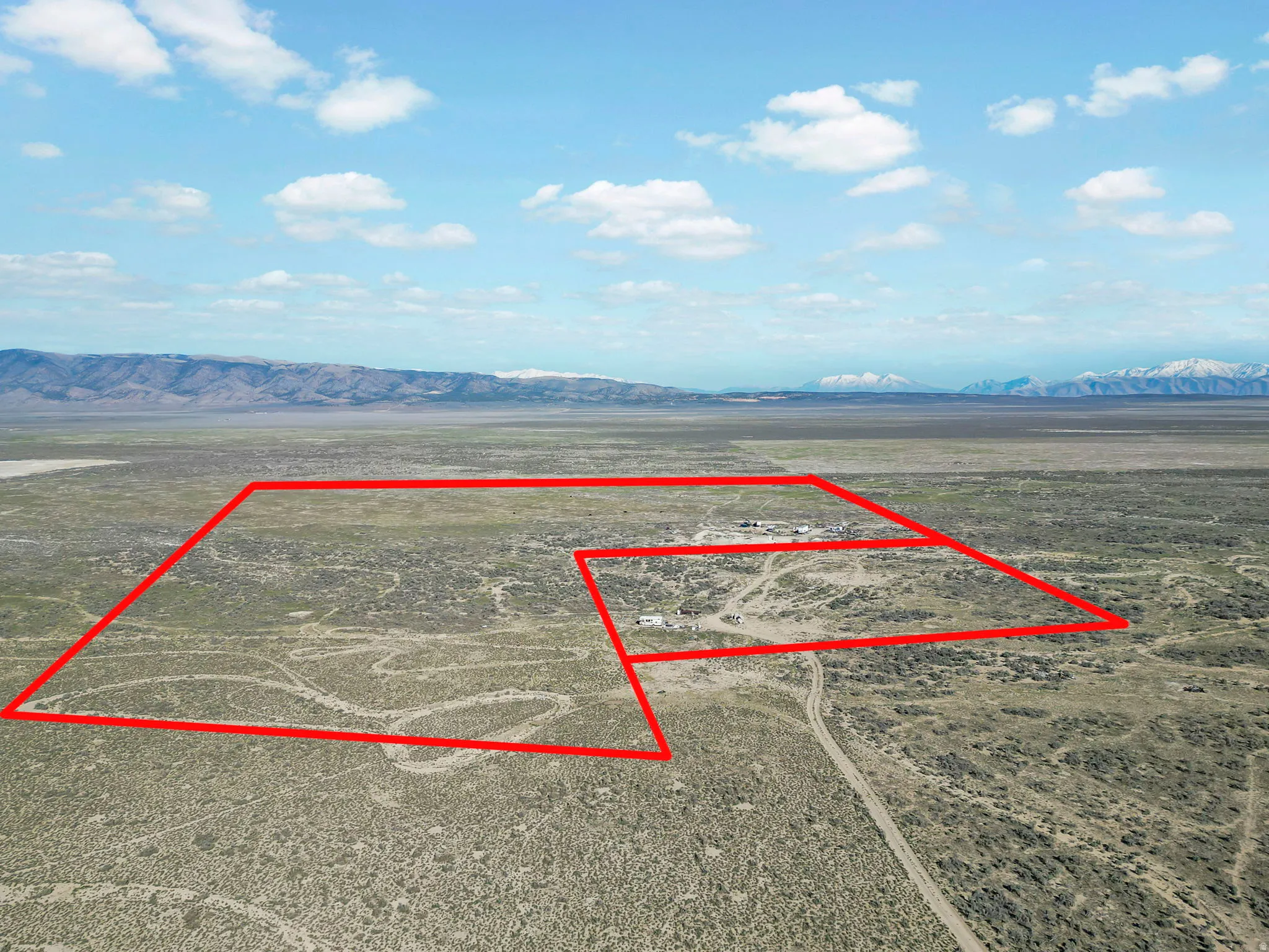 Expansive desert acreage featuring defined property boundaries, a distant mountain range, and scattered structures