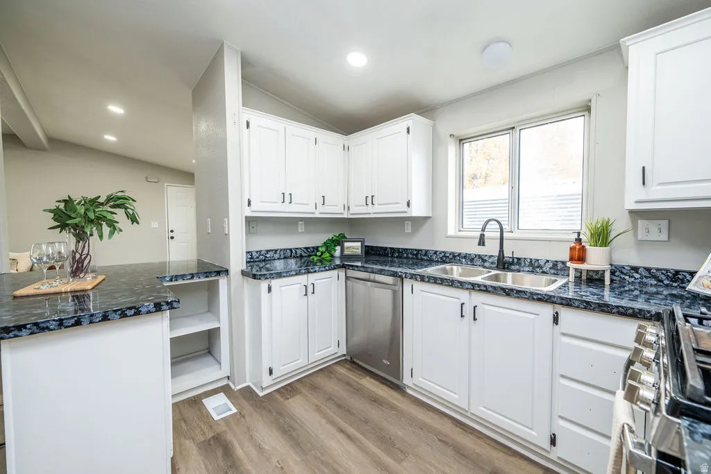 Kitchen with dark countertops, white cabinets, light wood finished floors, dishwasher, and vaulted ceiling
