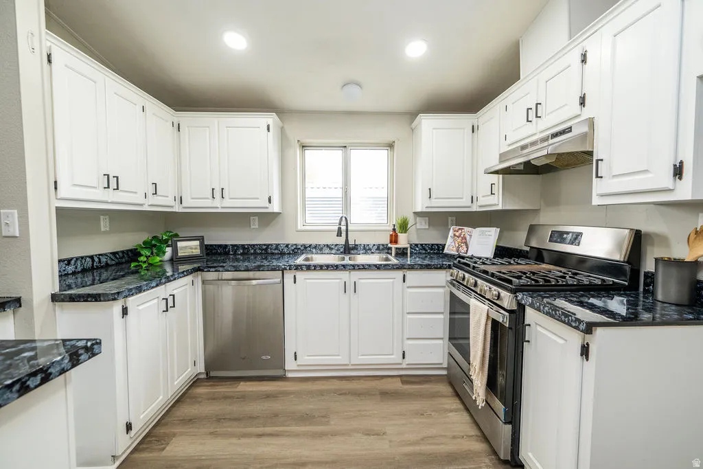 Kitchen featuring white cabinets, stainless steel appliances, light wood-type flooring, dark stone countertops, and recessed lighting