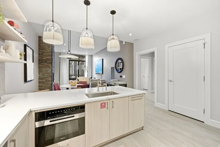 Kitchen with stainless steel oven, a peninsula, open shelves, pendant lighting, and light stone counters