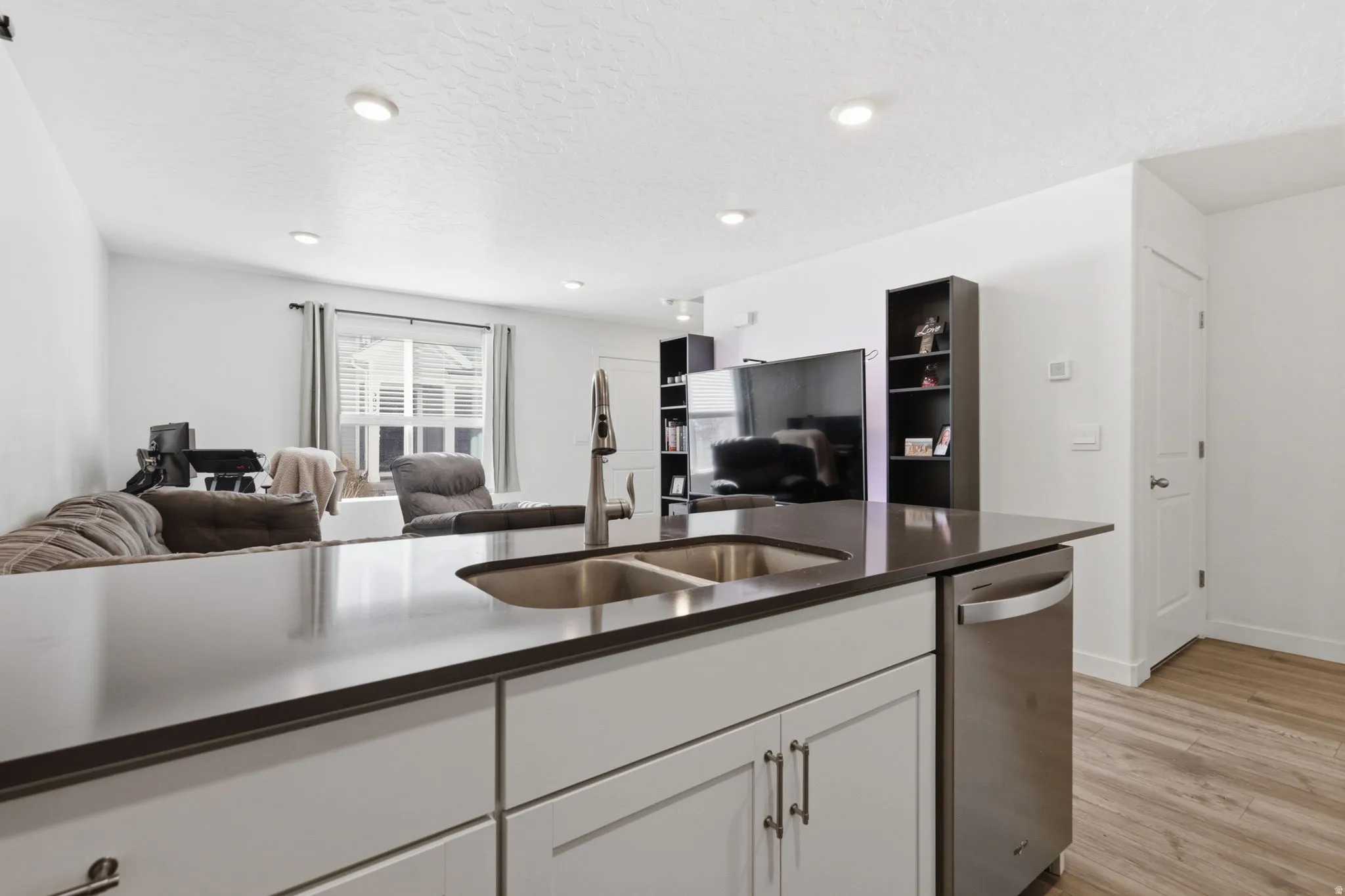 Kitchen with open floor plan, stainless steel dishwasher, light wood-style flooring, white cabinets, and a textured ceiling