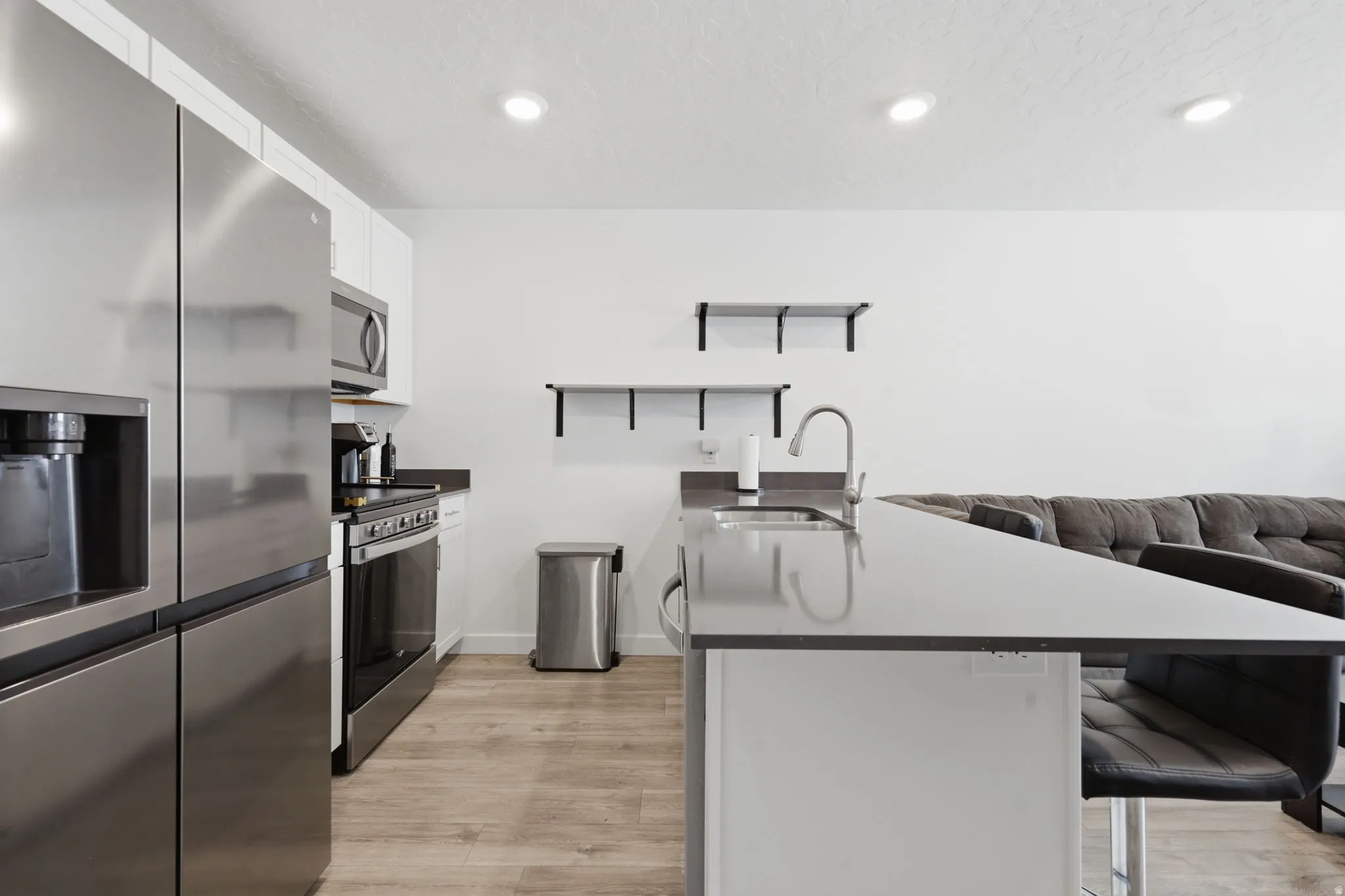 Kitchen featuring stainless steel appliances, a kitchen breakfast bar, white cabinets, light wood finished floors, and a peninsula