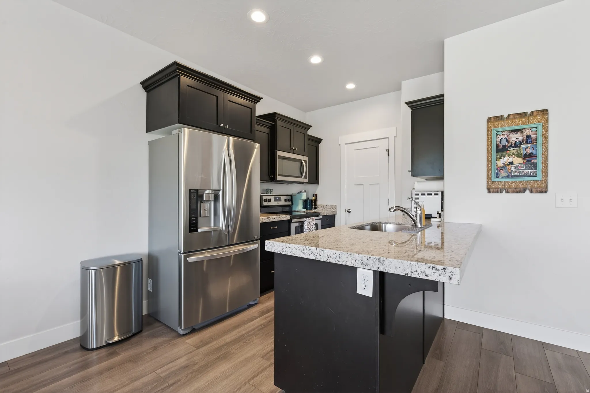 Kitchen featuring stainless steel appliances, a peninsula, dark cabinetry, dark wood-style floors, and a breakfast bar
