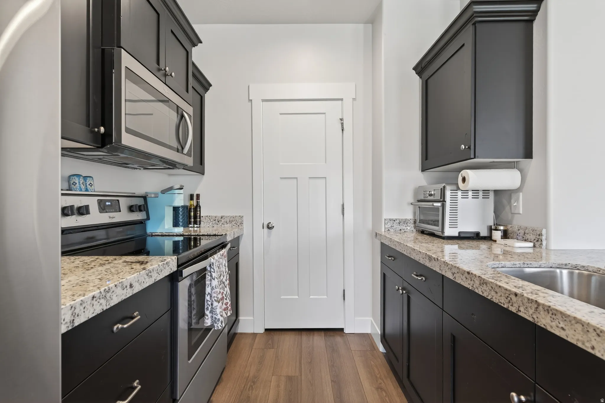 Kitchen with dark cabinets, stainless steel appliances, dark wood-style flooring, and light stone counters