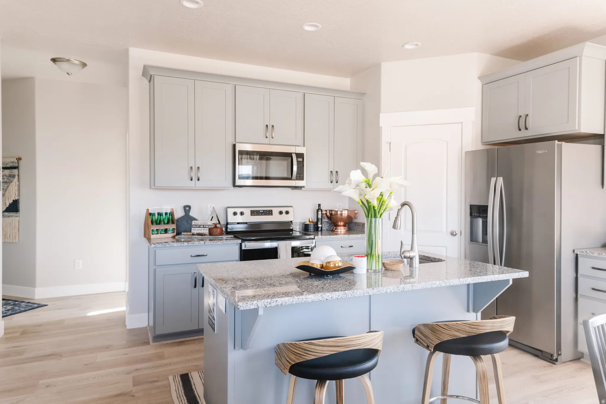 Kitchen with stainless steel appliances, light wood-style flooring, a kitchen bar, light stone counters, and recessed lighting