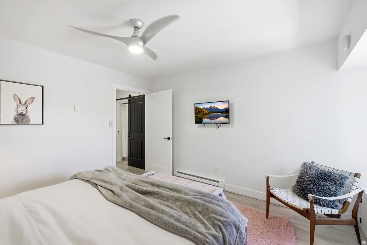 Bedroom with baseboard heating, light wood-style flooring, and ceiling fan