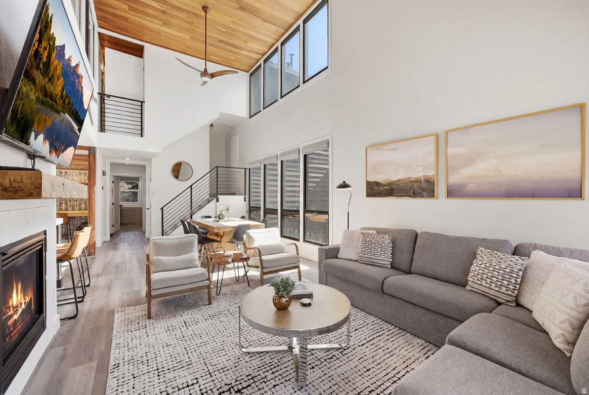 Living area with a glass covered fireplace, light wood-type flooring, ceiling fan, and a high wooden ceiling
