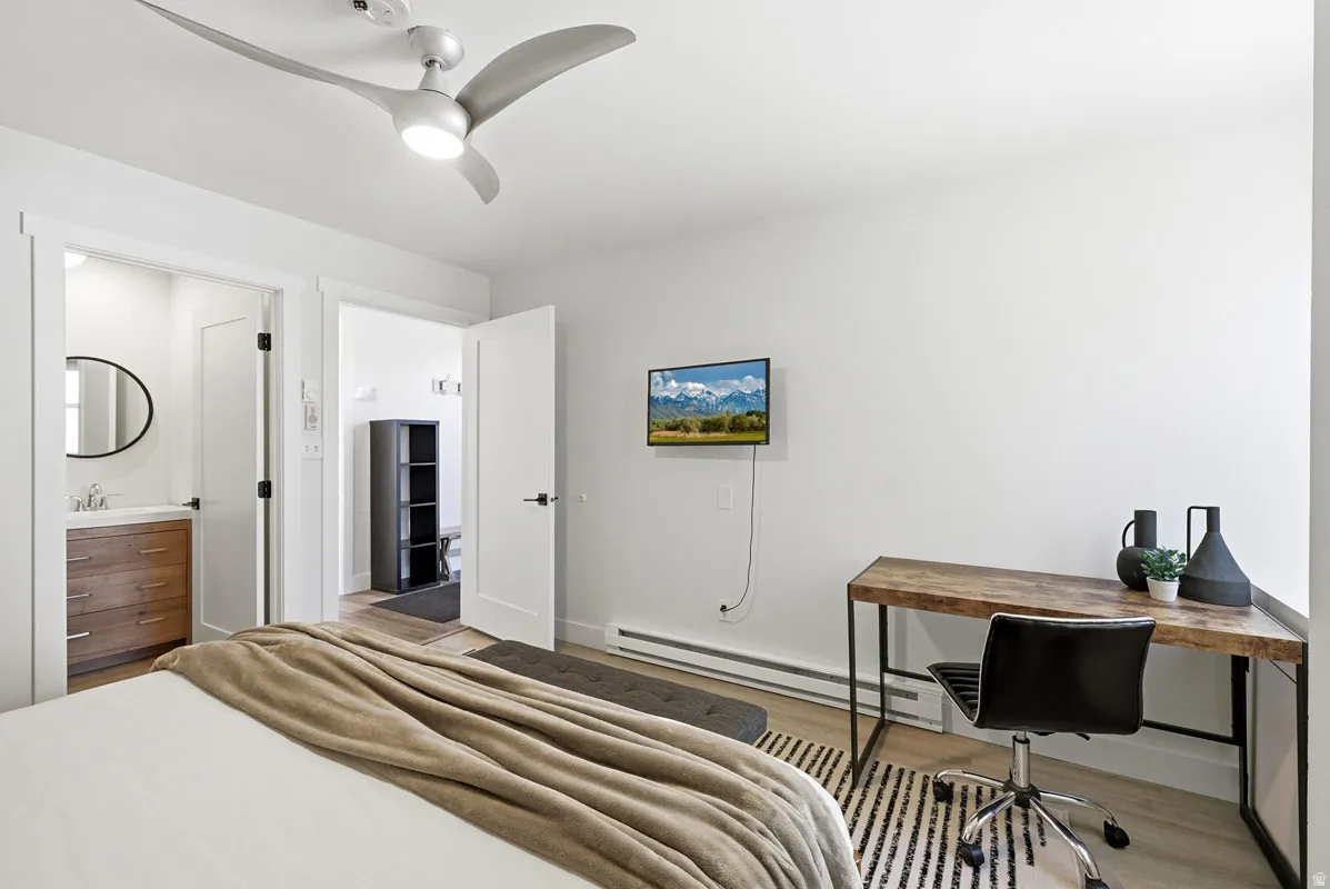 Bedroom featuring a baseboard heating unit, light wood-style flooring, a desk, ceiling fan, and ensuite bathroom