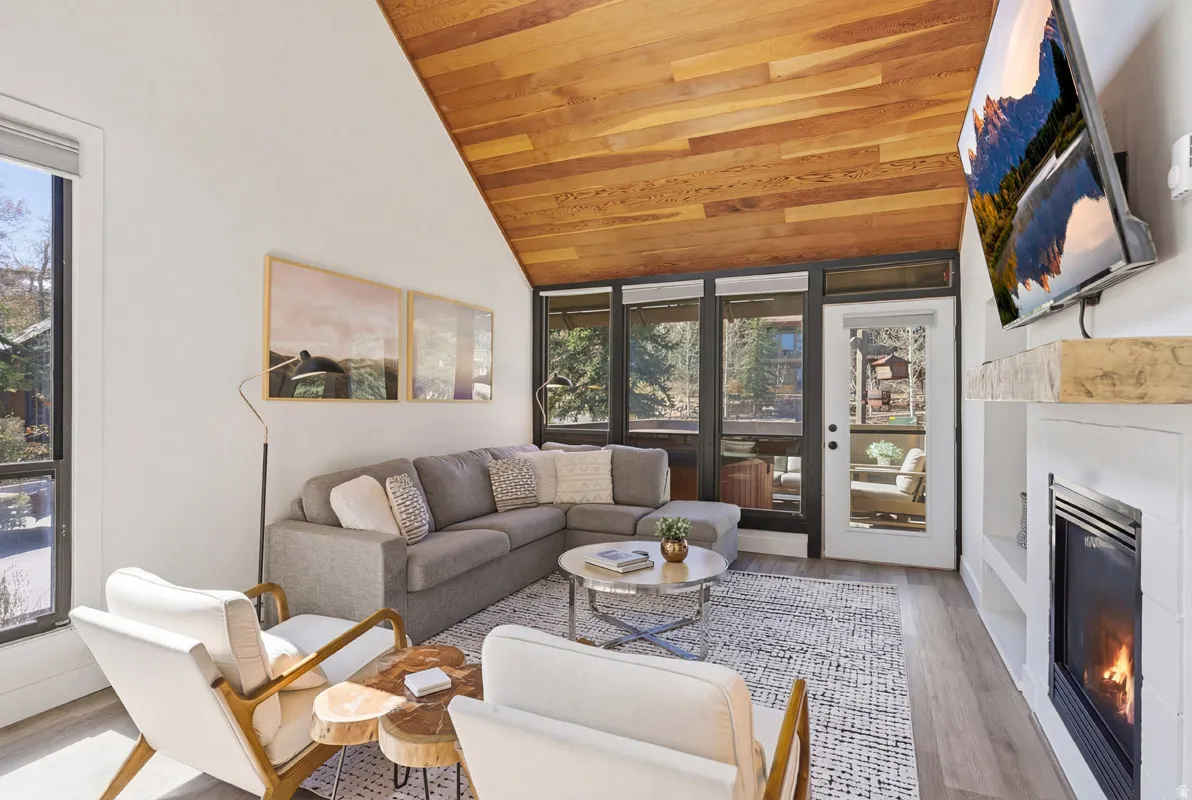 Living room with a glass covered fireplace, wood finished floors, plenty of natural light, and a vaulted wood ceiling