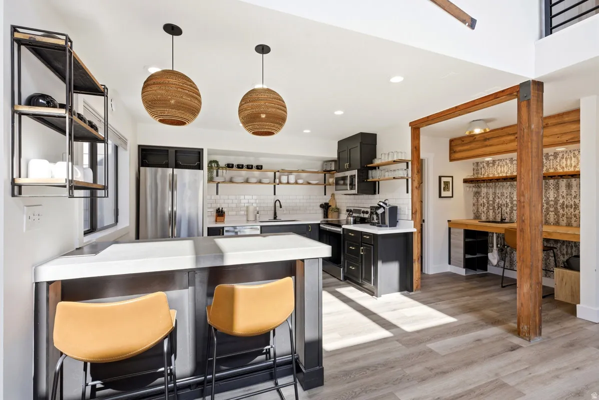 Kitchen with open shelves, a kitchen bar, a peninsula, stainless steel appliances, and light wood-style floors