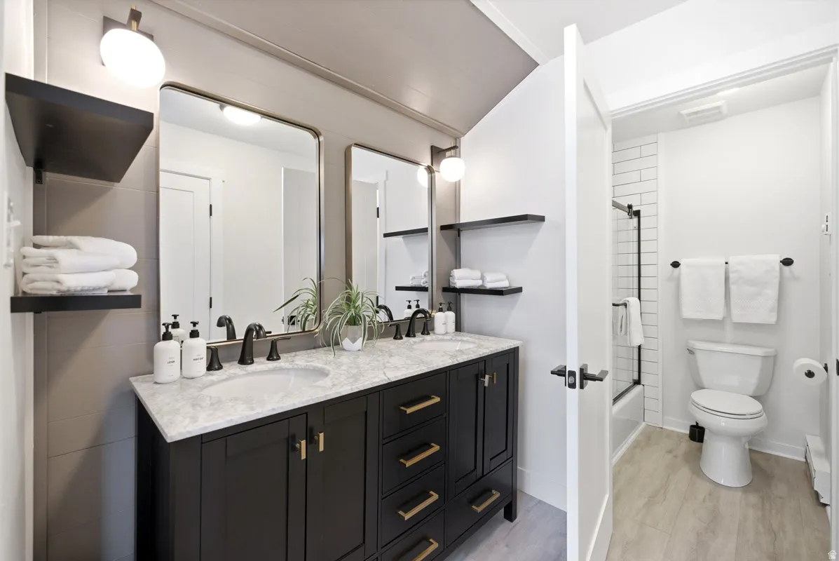 Bathroom with double vanity, shower / bathtub combination, light wood-type flooring, and baseboard heating