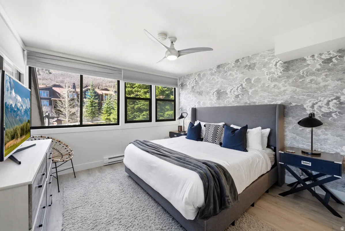 Bedroom with light wood-style flooring, ceiling fan, and a baseboard heating unit