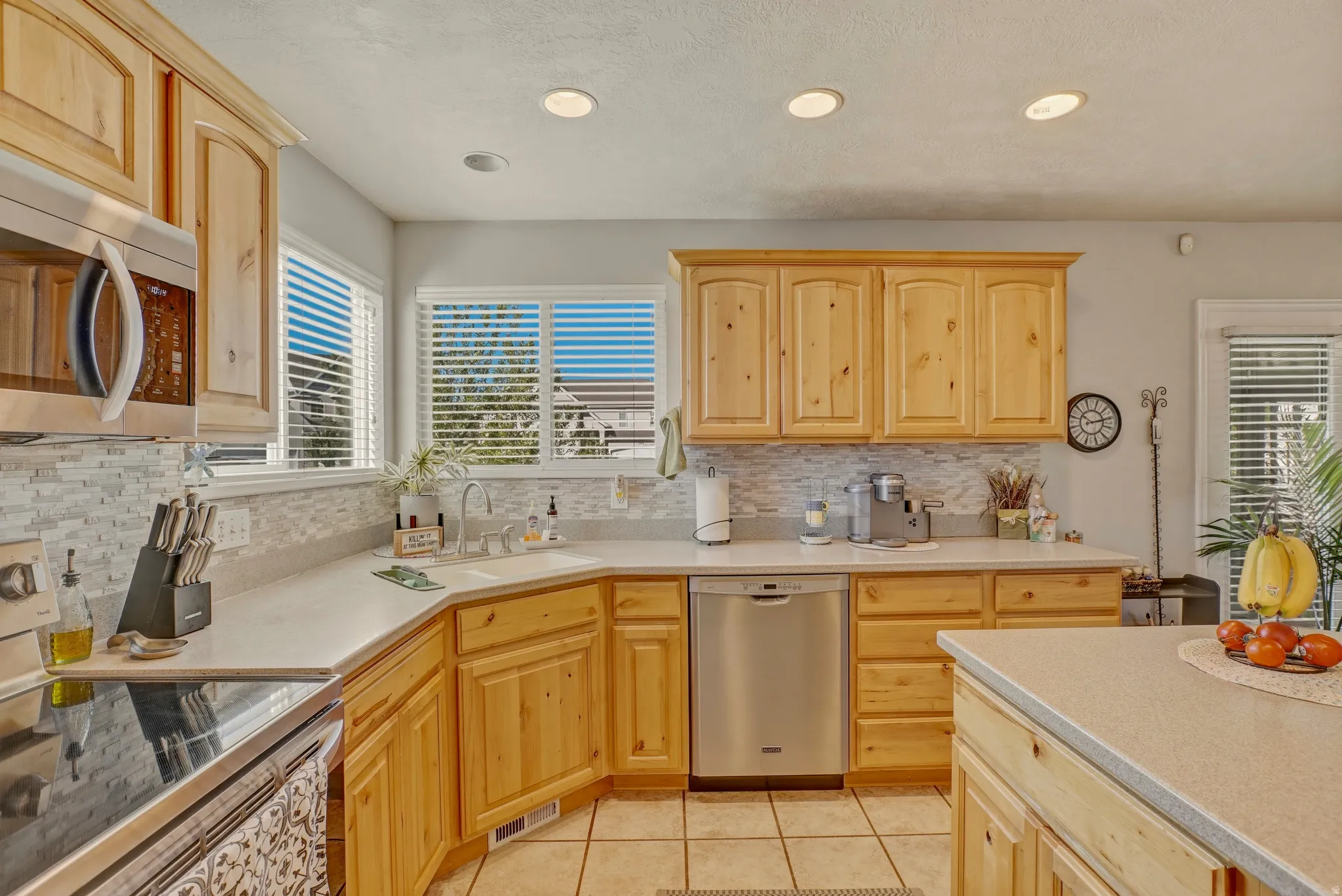 Kitchen with stainless steel appliances, light wood finish cabinets, light tile patterned floors, recessed lighting, and decorative backsplash