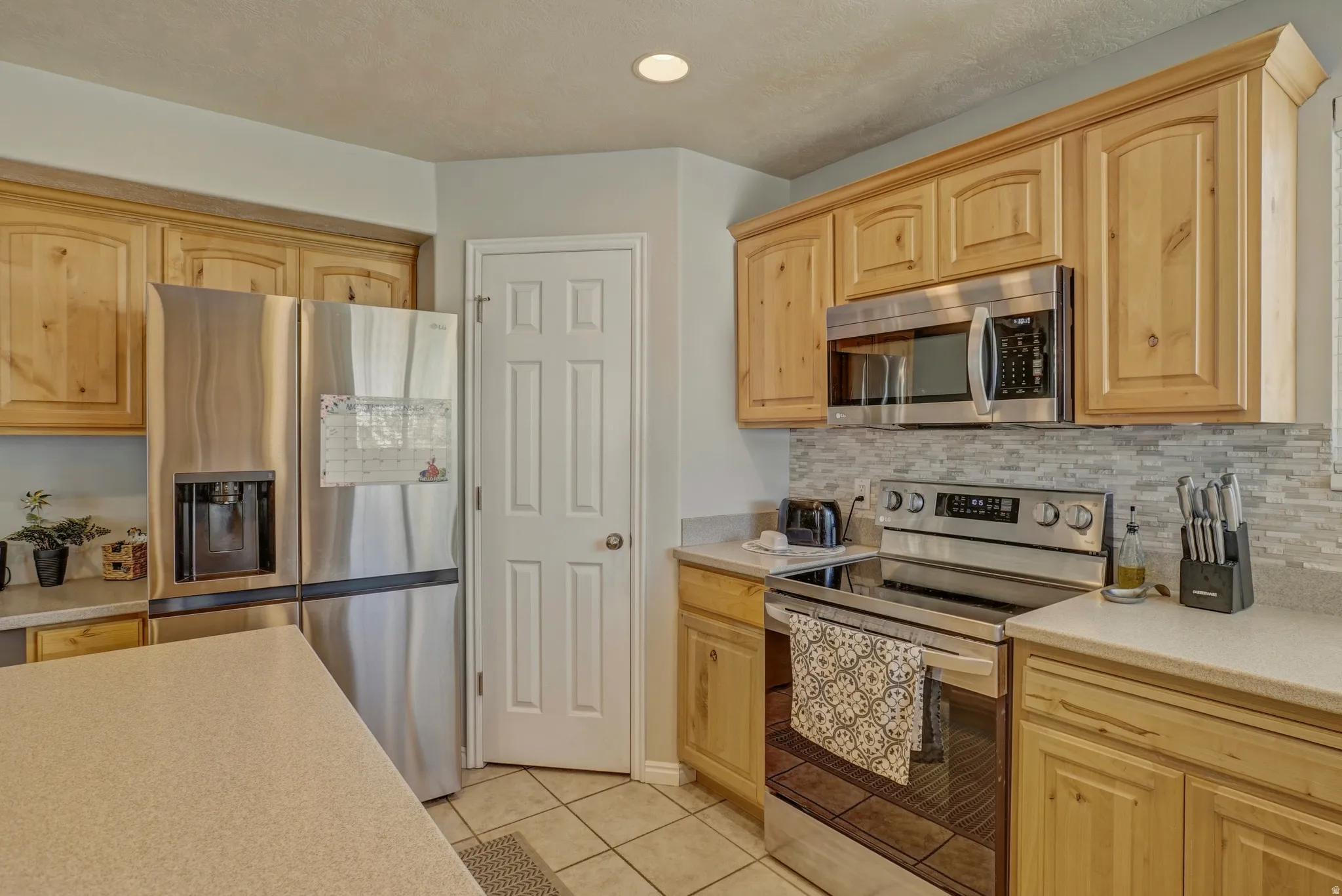 Kitchen with stainless steel appliances, light wood finish cabinetry, light tile patterned floors, and tasteful backsplash