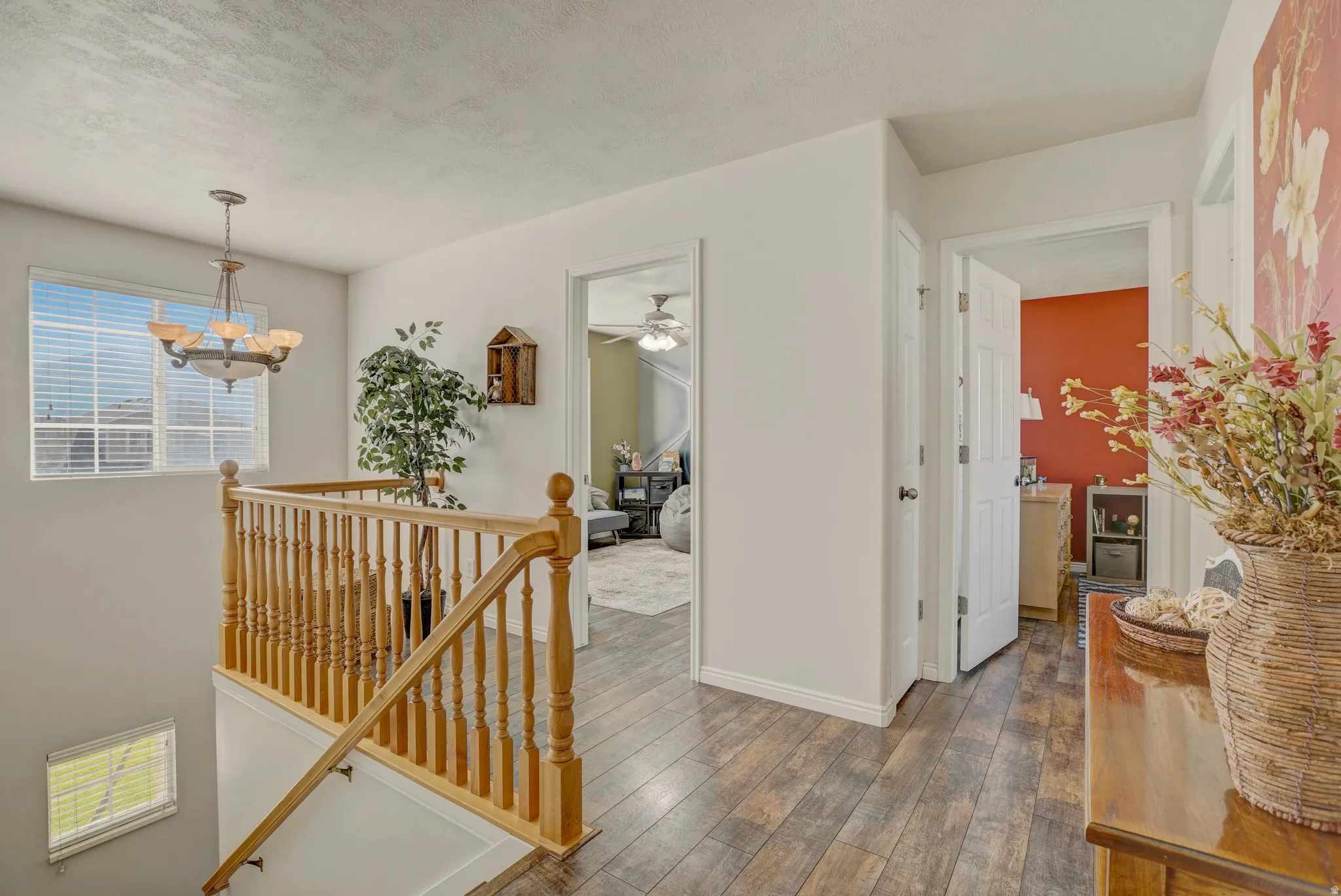 Hallway featuring an upstairs landing, hardwood / wood-style flooring, suspended lighting, and a textured ceiling