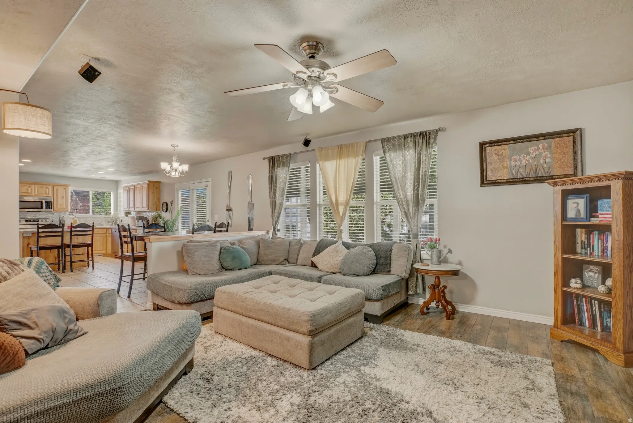 Living room with a chandelier, ceiling fan, light wood-style flooring, and a textured ceiling