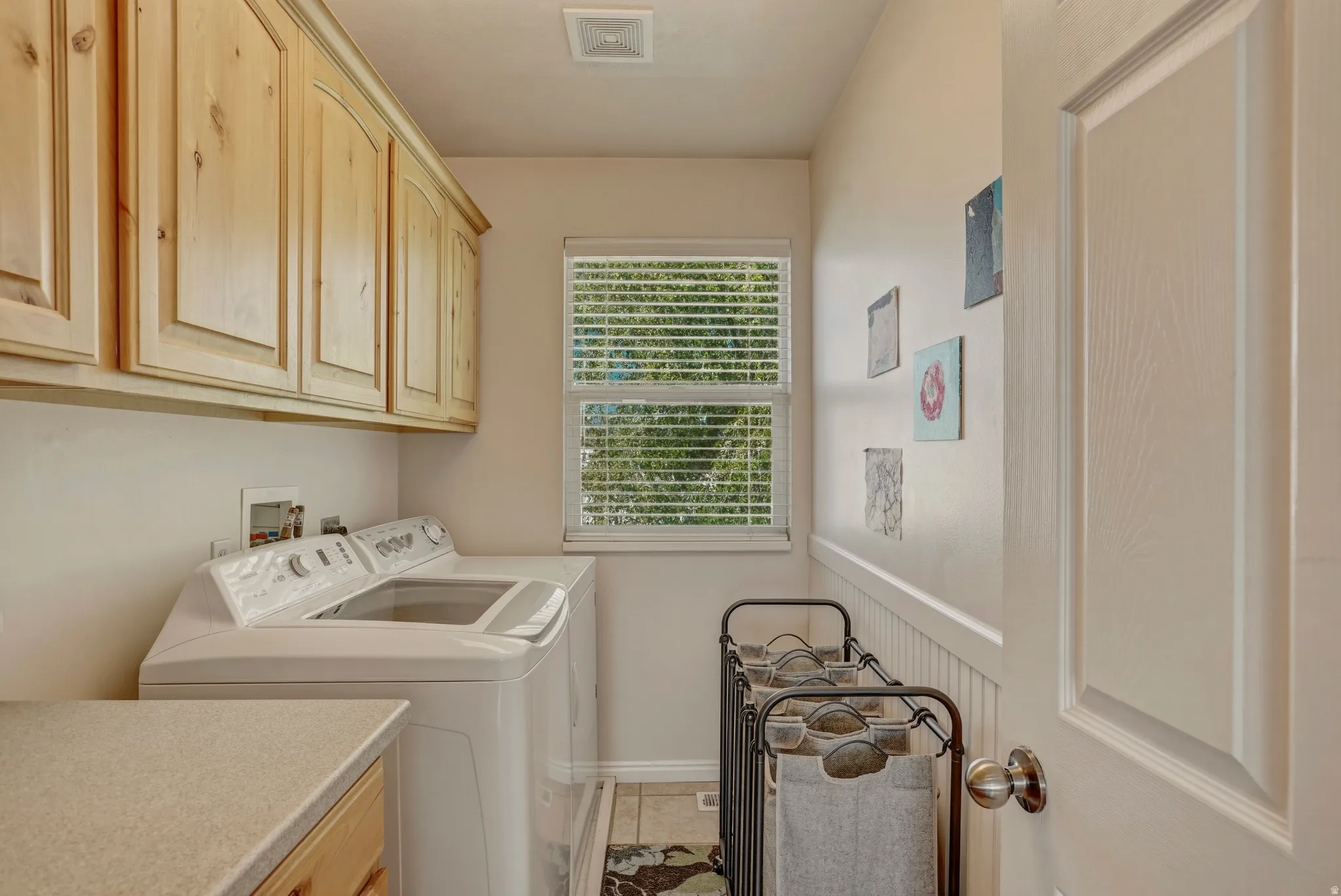 Laundry area with cabinet space, separate washer and dryer, wainscoting, and light tile patterned floors