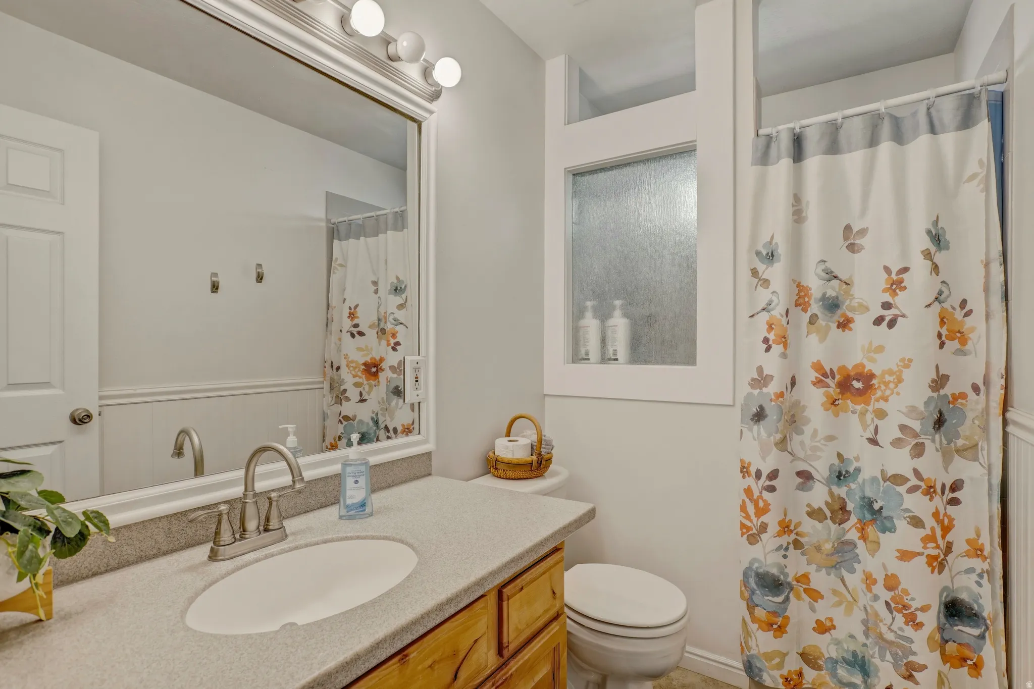 Full bath featuring vanity, a shower with curtain, a wainscoted wall, and a decorative wall