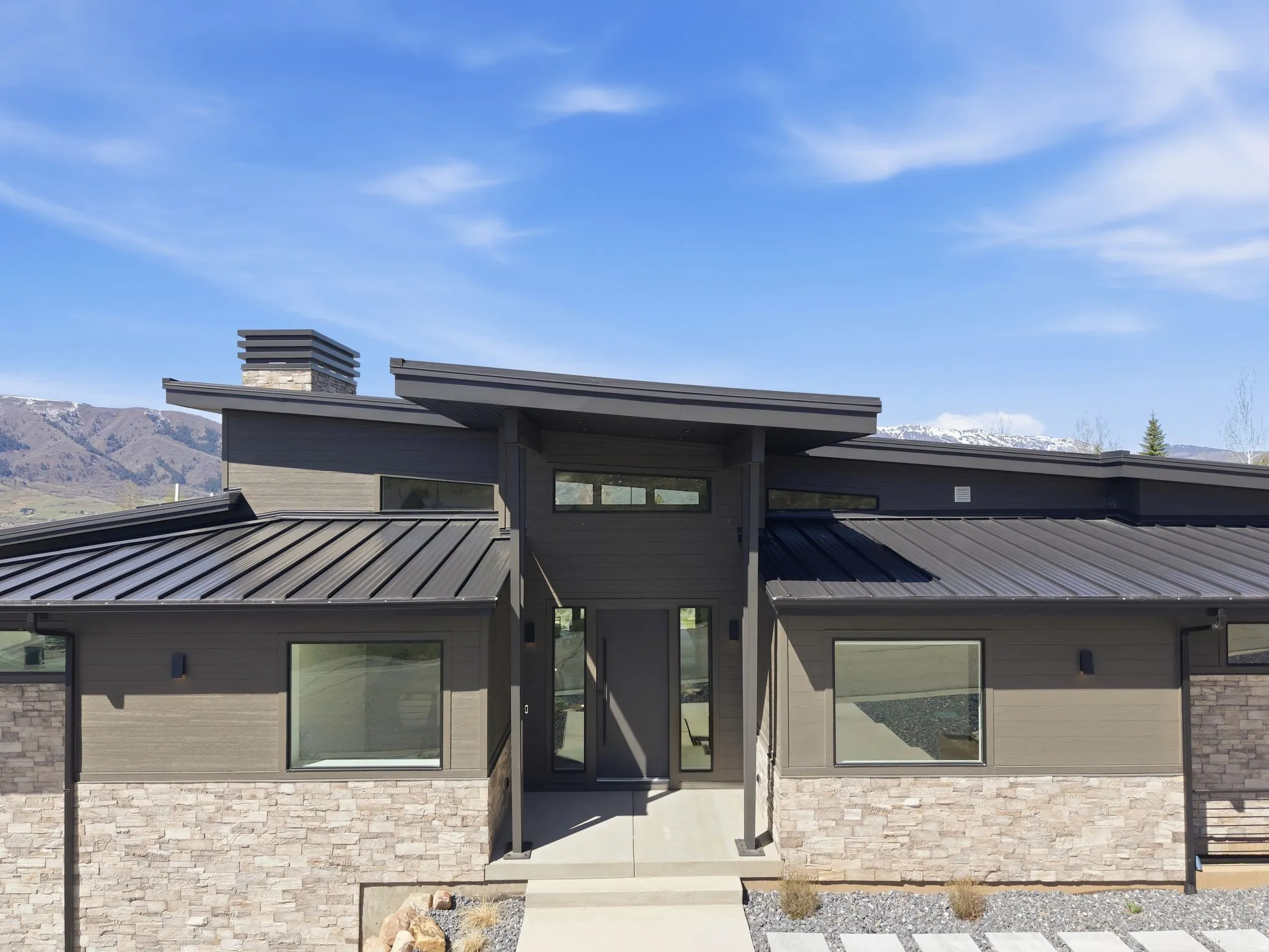 View of front of property featuring stone siding, a standing seam roof, and a chimney