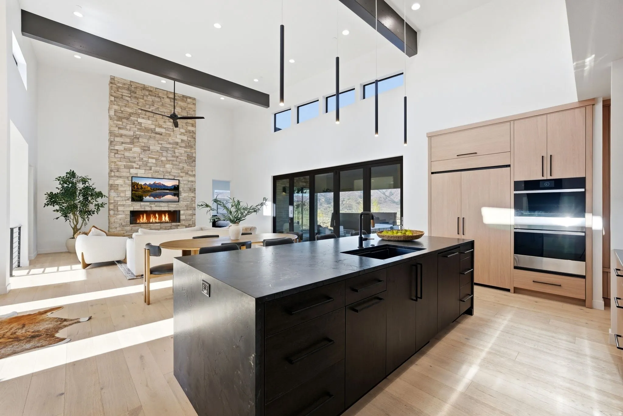 Kitchen featuring a large island with sink, a stone fireplace, light wood-type flooring, stainless steel double oven, and modern cabinets