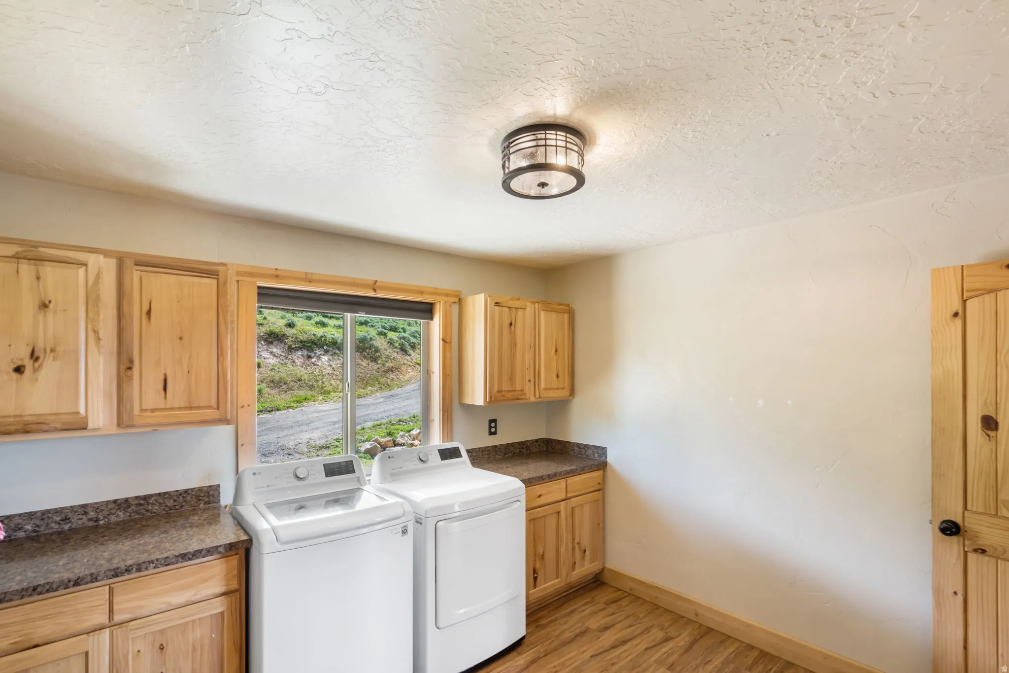 Laundry room with light wood-style floors, washing machine and clothes dryer, cabinet space, and a textured ceiling