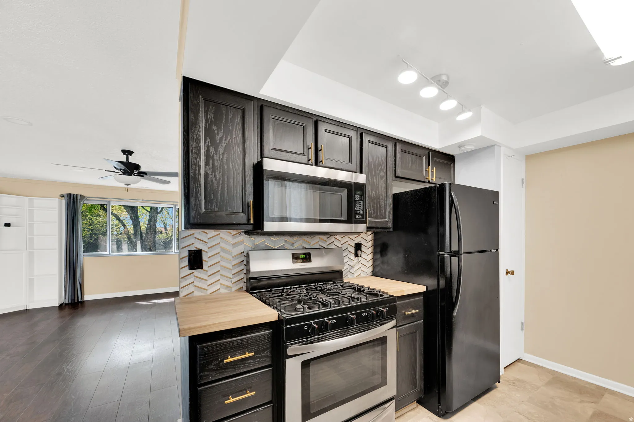 Kitchen with stainless steel appliances, ceiling fan, wooden counters, and tasteful backsplash