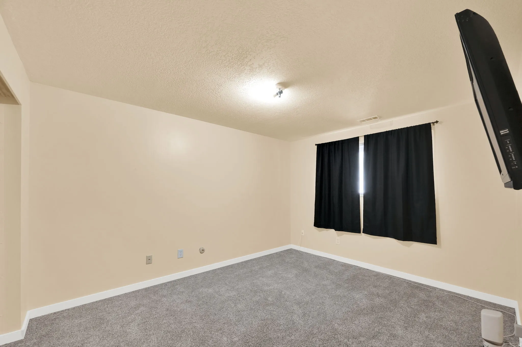 Carpeted spare room featuring a textured ceiling and baseboards