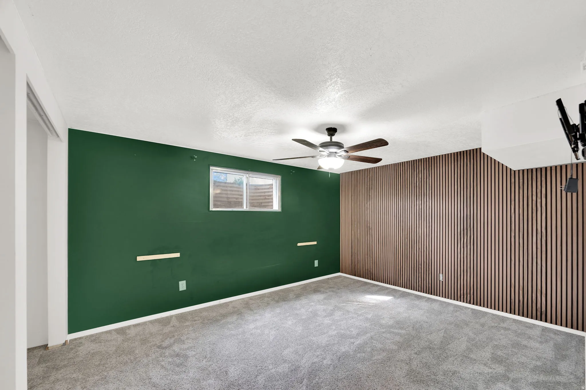 Unfurnished bedroom featuring a textured ceiling, carpet, an accent wall, wooden walls, and ceiling fan