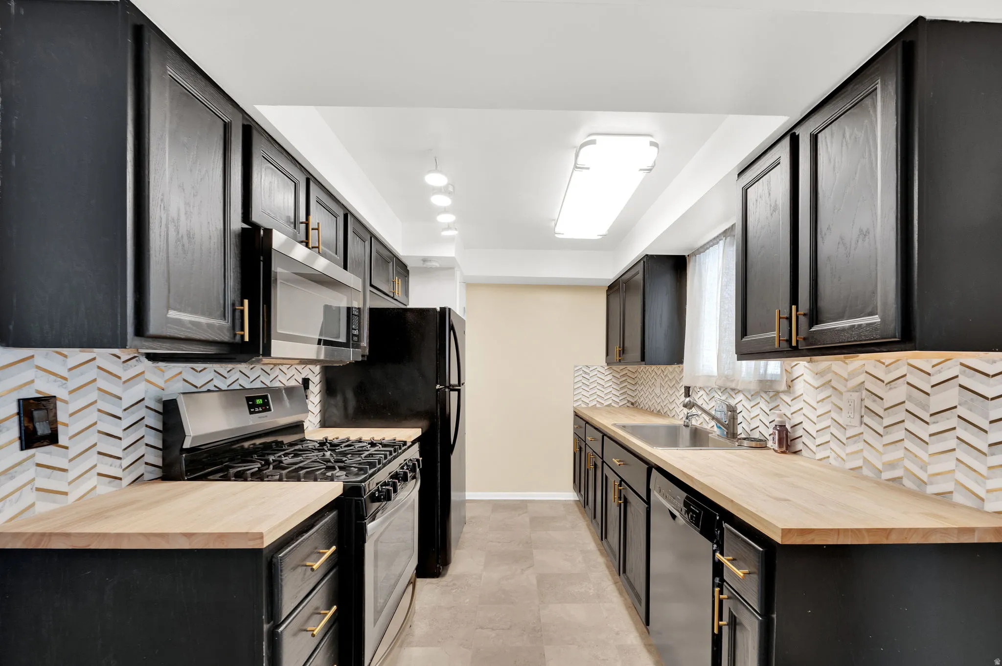 Kitchen featuring dark cabinets, stainless steel appliances, wood counters, and backsplash