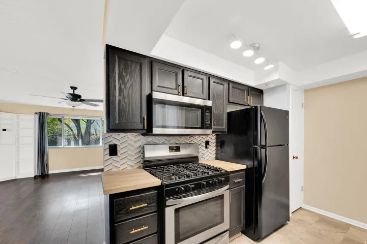 Kitchen with stainless steel appliances, ceiling fan, wooden counters, and tasteful backsplash