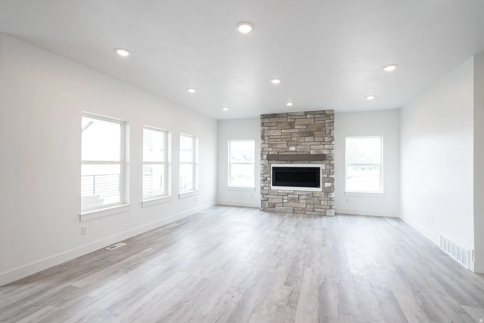 Unfurnished living room featuring a stone fireplace, light wood-style flooring, and recessed lighting