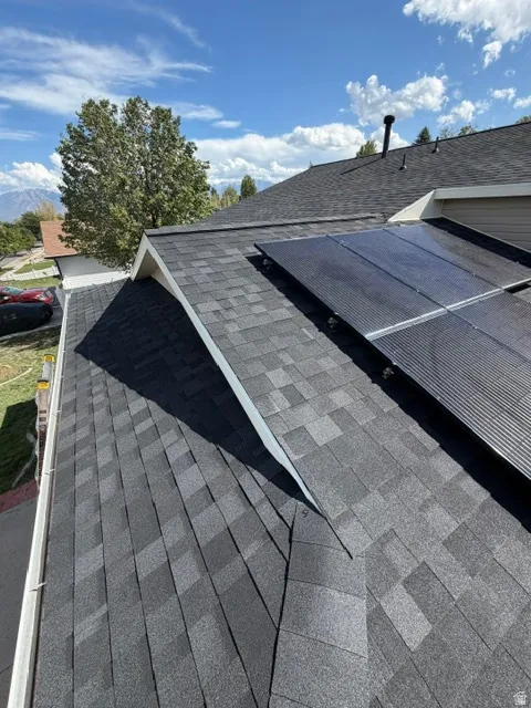 Asphalt shingle roofing with installed solar panels and a visible gutter system