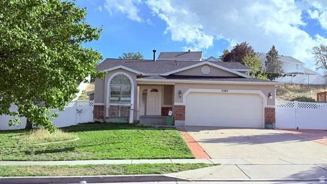 Stucco exterior with brick detailing, arched window feature, attached two-car garage, concrete driveway, and white picket fencing