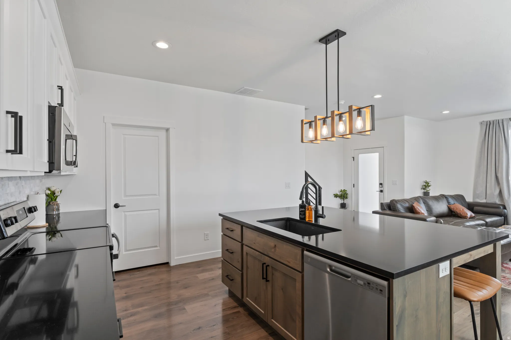 Kitchen featuring stainless steel appliances, a kitchen island with sink, dark wood-type flooring, open floor plan, and decorative light fixtures