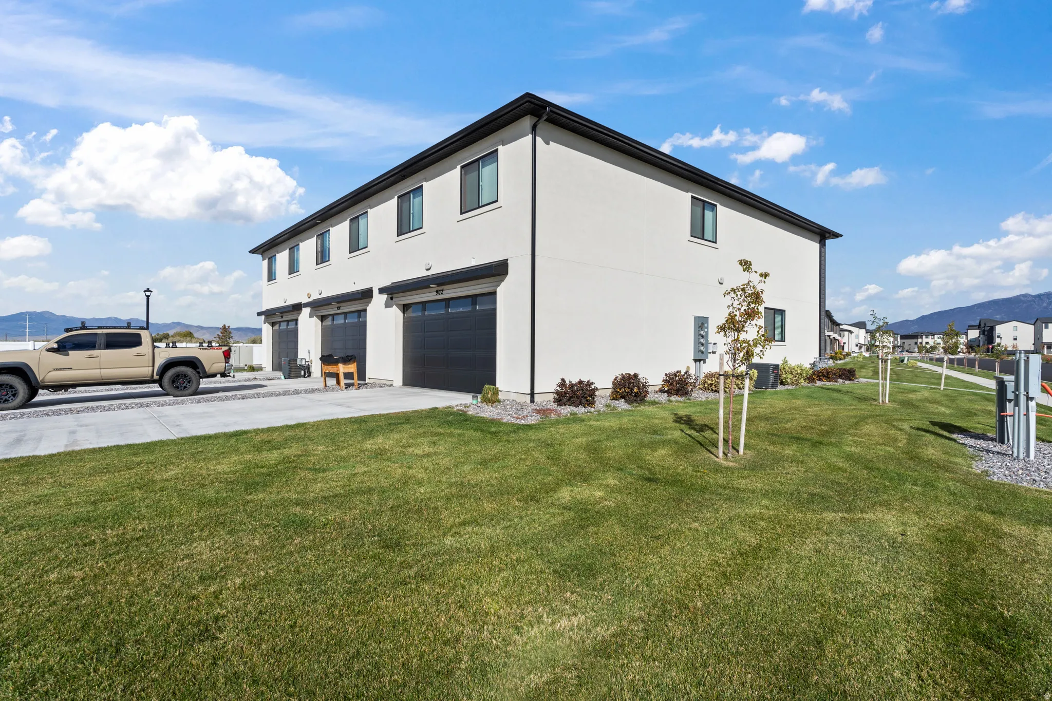 View of side of property featuring a mountain view, a garage, concrete driveway, stucco siding, and a lawn
