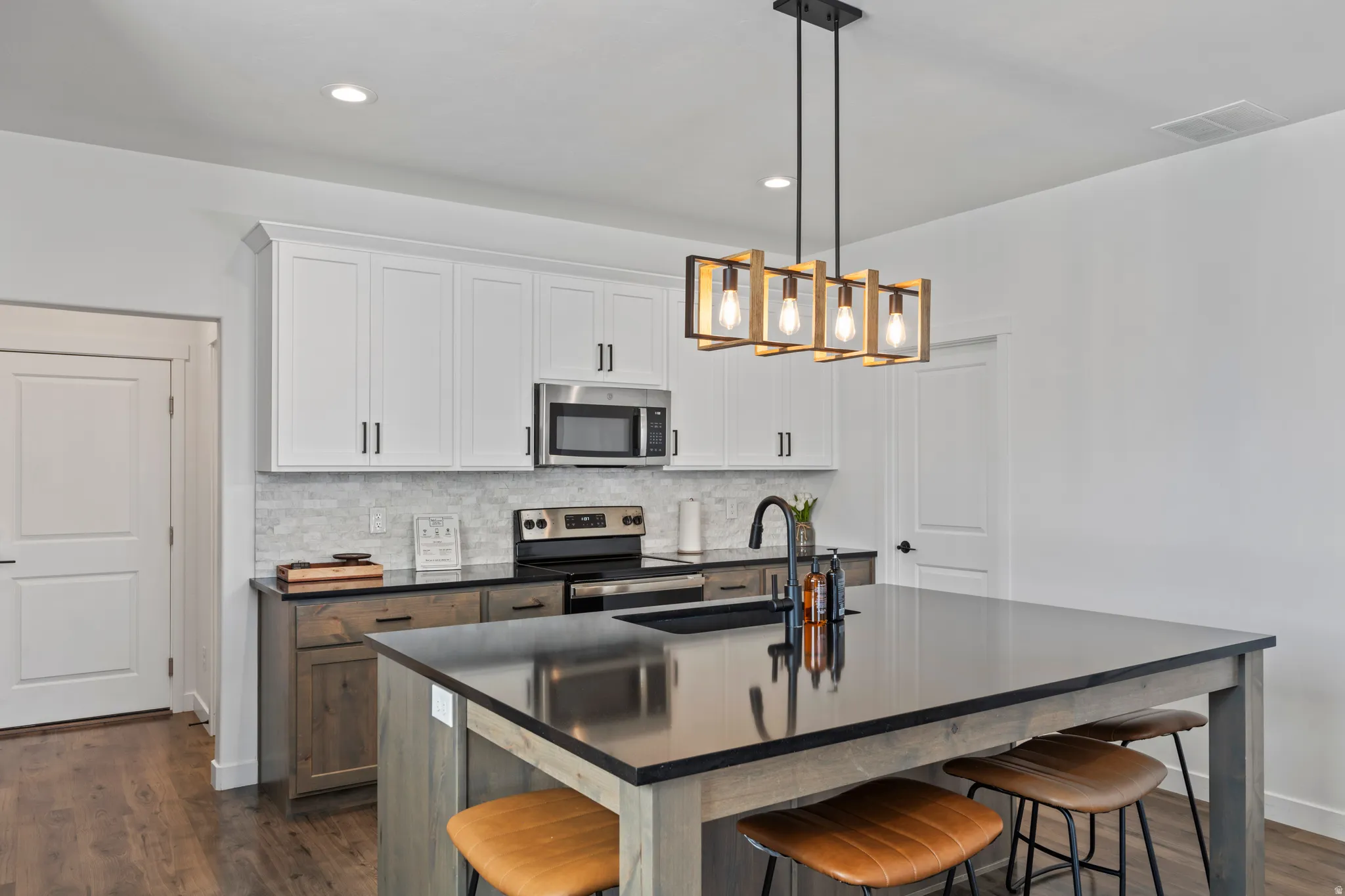 Kitchen featuring a kitchen breakfast bar, dark wood finished floors, stainless steel appliances, tasteful backsplash, and two tone cabinetry