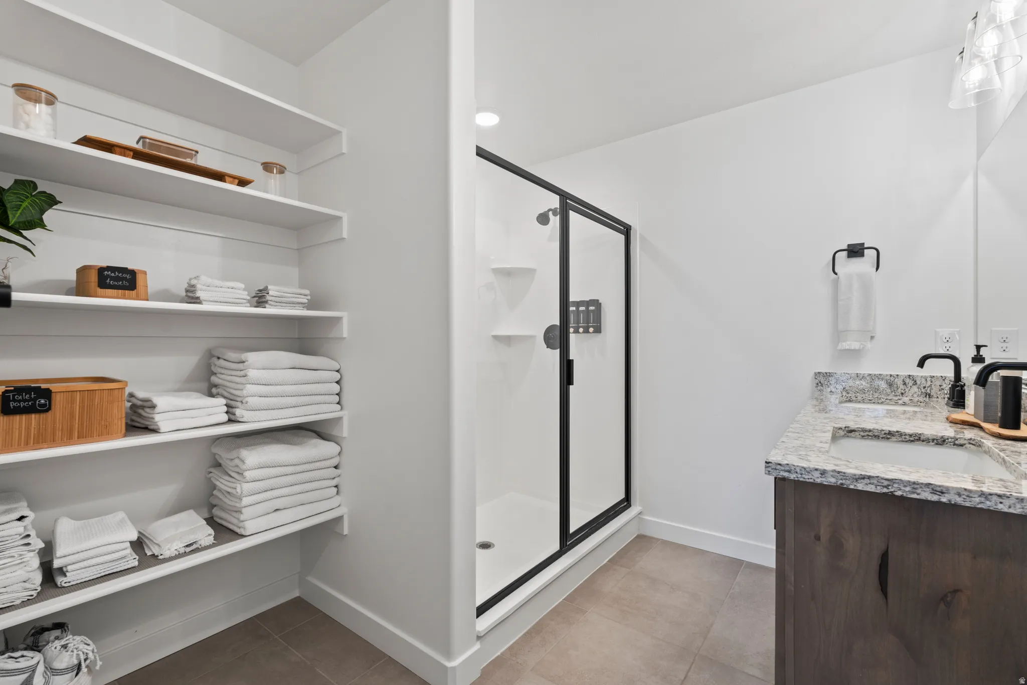 Bathroom featuring a shower stall, double vanity, light tile patterned flooring, and a closet