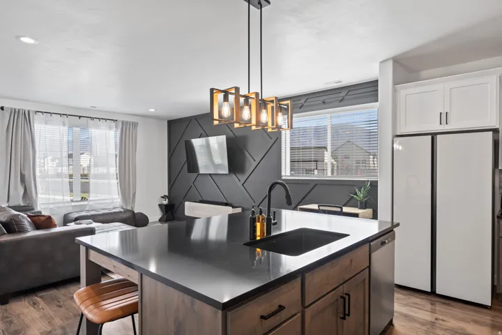 Kitchen featuring freestanding refrigerator, dark wood-style flooring, an island with sink, and pendant lighting
