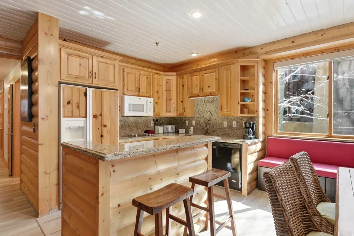 Kitchen with light wood finish cabinets, light stone counters, a center island, dishwasher, and white microwave